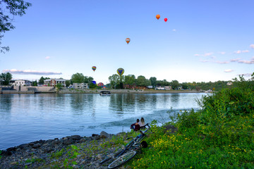 Gatineau, Quebec, Canada - September 15th, 2019:  romantic couple watching hot air balloons festival on a shore during summer came by bike
