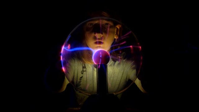 Pretty curious girl moves her fingers on the surface of the plasma tesla ball and watches for changes in condition