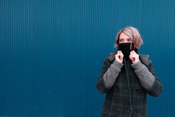 COVID-19 Pandemic Coronavirus A young woman on a blue wall backgound in a protective mask for the spread of the SARS-CoV-2 disease virus. Girl with a black mask on her face against coronavirus disease