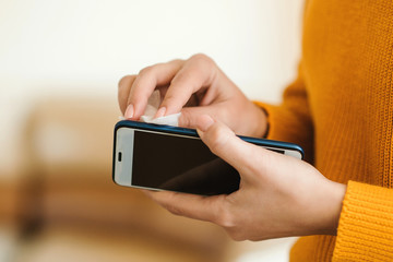 Woman cleaning mobile phone with antiseptic wet wipe. Personal hygiene and coronavirus quarantine concept.
