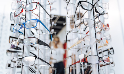 Row of glasses at an opticians. Eyeglasses shop. Stand with glasses in the store of optics. Woman's hand gives glasses to a man. Presenting spectacles