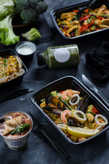 Healthy food and diet concept, restaurant dish delivery. Take away of fitness meal. Weight loss nutrition in boxes. Seafood Paella in black box. Tiramisu dessert