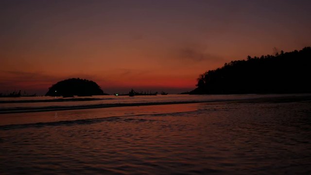 soft sea wave breaking sand beach, silhouette tree mountain on right, island in the ocean, long tail fishing boat parking in water, at twilight colorful orange evening time after sunset