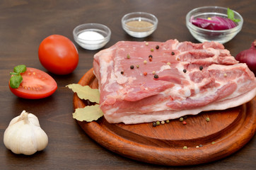 piece of pork meat on a wooden board and vegetables on the table