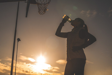 Silhouette of a young woman drinking water during morning workout