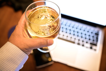 Successful young businessman holding a glass of beer at the end of his working day. Selective focus. View from above End of the work day, time to relax. Technology concept