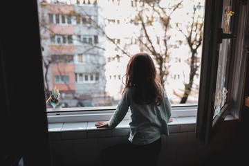 Little girl watching on the window during Covid-19 home quarantine.