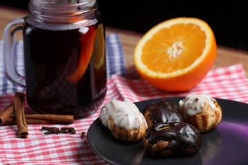 Glass of mulled wine, eclairs on a black plate, orange , cinnamon and cloves isolated on a black background.