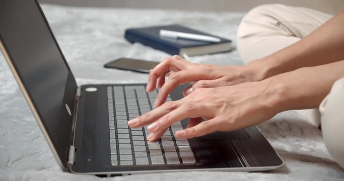 Close up female hands typing on a laptop keyboard. No face woman freelancer or student working writing post comments in social networks sitting on sofa at home.