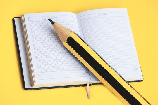 Paper notepad and huge pencil on the yellow background.