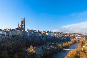 Naklejka premium Beautiful panorama view of Fribourg (Freiburg) old town on a sunny winter day from Zaehringen Bridge with the tower of Fribourg Cathedral and Sarine River flowing below, Switzerland