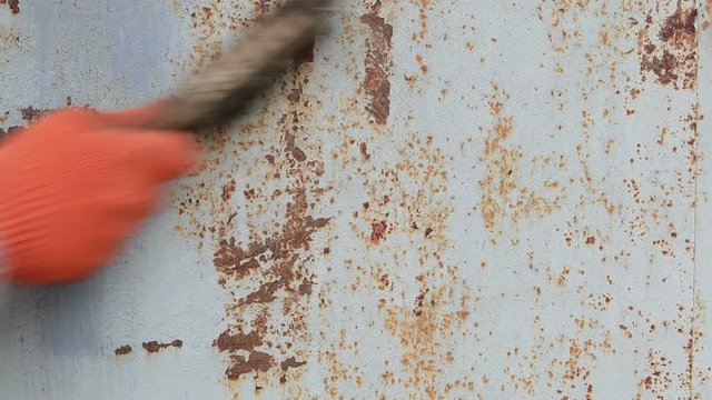 A man brushes metal doors from rust before painting.