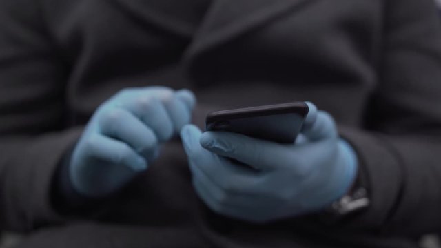 Man in the coat in the medical gloves texting while being in the subway during the pandemic coronavirus