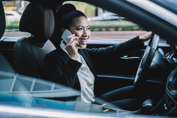 Happy young Asian female manager speaking on smartphone in car