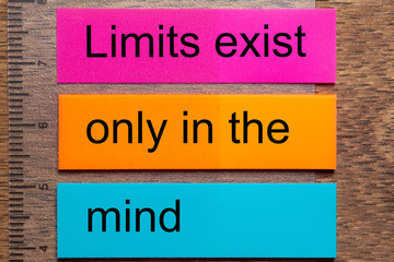 Three bookmark stickers with the words Limits exist only in the mind, on a dark natural wooden table