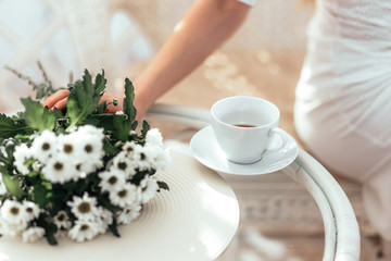 A Cup of tea and a bunch of chrysanthemums are on the glass table.