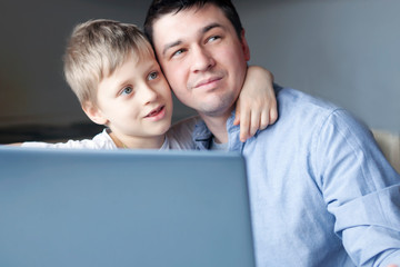 The boy and dad are hugging and looking one way. Son hugs dad. Family happiness. Dad is working on...