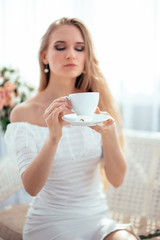 The girl drinks morning tea and enjoys life, admiring a bouquet of flowers .