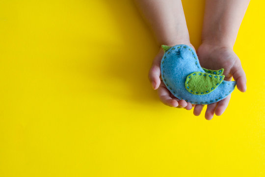 Hand Finish. Blue Easter Bird From Felt Fabric In The Hands Of A Child On A Yellow Background. Flat Lay,overhead,top View,copy Space, Place For Text