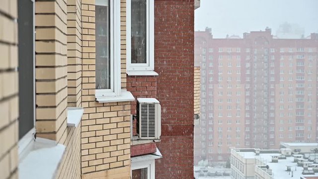 Slow motion footage of snow falling along brick facade of high rise building