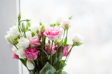 Defocused view. Bouquet of pink and white eustoma in a glass vase on the windowsill of the loggia. Flowers in a vase on the windowsill of the balcony.