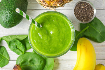 Healthy green smoothie in a glass with a straw made of spinach, pineapple, avocado, banana and chia seeds. top view