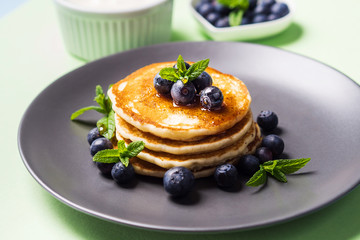 Stack of home made pancakes served with fresh berries and maple syrup on mint green pastel background. Simple and delicious breakfast