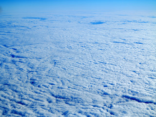 view from the wing of the plane to the ground and to the blue cloudy sky