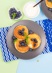 Pancakes served with fresh blueberries on gray plate over geometrical background. Healthy home made breakfast concept