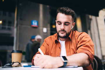 Young focused man writing notes down