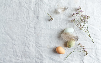 An arrangement of Easter eggs, feathers and dried flowers on linen background. Flat lay. Copy space