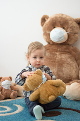 Child playing with his sick teddy bears wearing medical mask against viruses. Role playing, child playing doctor with plush toy. Children and flu, coronavirus illness concept. Selective focus