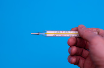 Man holds a medical thermometer in his hand on a blue background