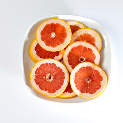 Fototapeta na wymiar Sliced grapefruit rings in white plate on a pink background .