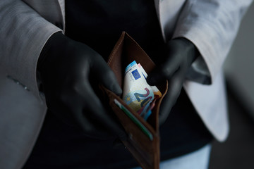 Man holding a wallet with money euro in hand in black medical gloves