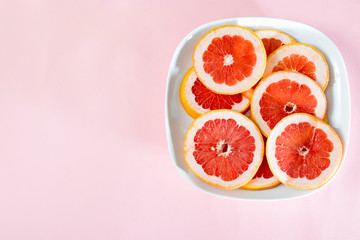 Sliced grapefruit rings in white plate on a pink background .