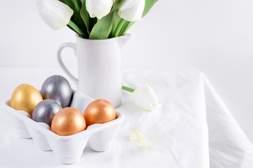 Greeting Easter card with handmade painted bright eggs and bouquet of fresh tulips flowers on a light textile background.