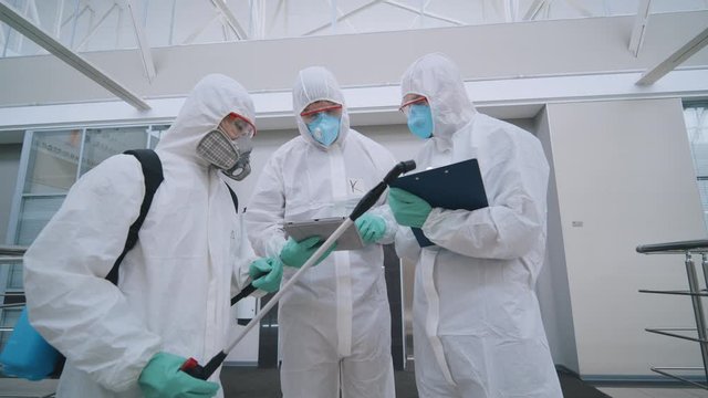 Covid-19 coronavirus epidemic. Three people in protective suits in office to disinfect