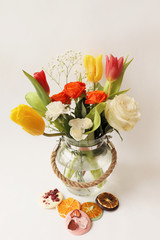 Composition of a bouquet of spring flowers in a glass vase, colored chocolate and dried fruits on a white background. Selective focus.