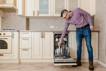 Young man hand put dishes in open dishwasher