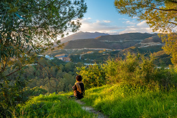 woman relaxing and meditating at sunset on green hill with beautiful view of countryside and mountains