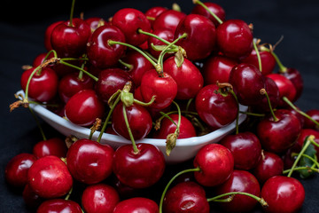 Red cherries on black background coming out and hanging from the plate