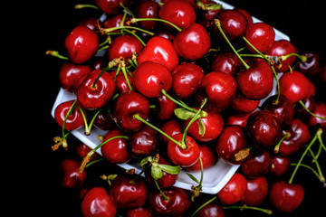 Obraz na płótnie Canvas Red cherries on black background coming out and hanging from the plate