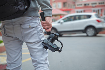 An unidentified man holding gimbal a camera stabilizer . Man holding gimbal stabilizer outdoor. Gimbal Operator with black equipament - Stabilizer and camera filmmaking