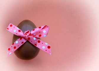 Chocolate egg with a bow on pink background
