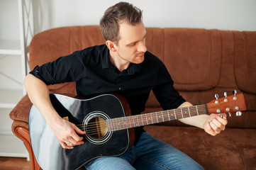 A guy tunes a guitar on the couch