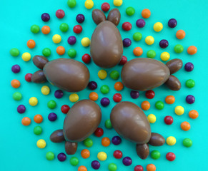 Top view of chocolate eggs in the form of rabbits and colored candies on a green background