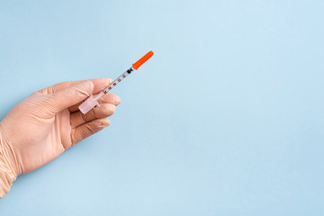 Woman's hands in the medical gloves holds syringe on a light blue background.