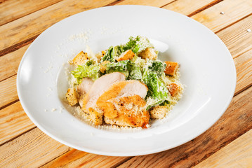 Fresh caesar salad in white plate, wooden background