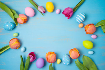 Easter holiday background with easter eggs and tulip flowers on wooden table. Top view from above